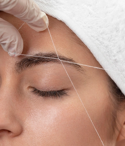 mujer haciendo la depilación de las cejas con hilo a una clienta